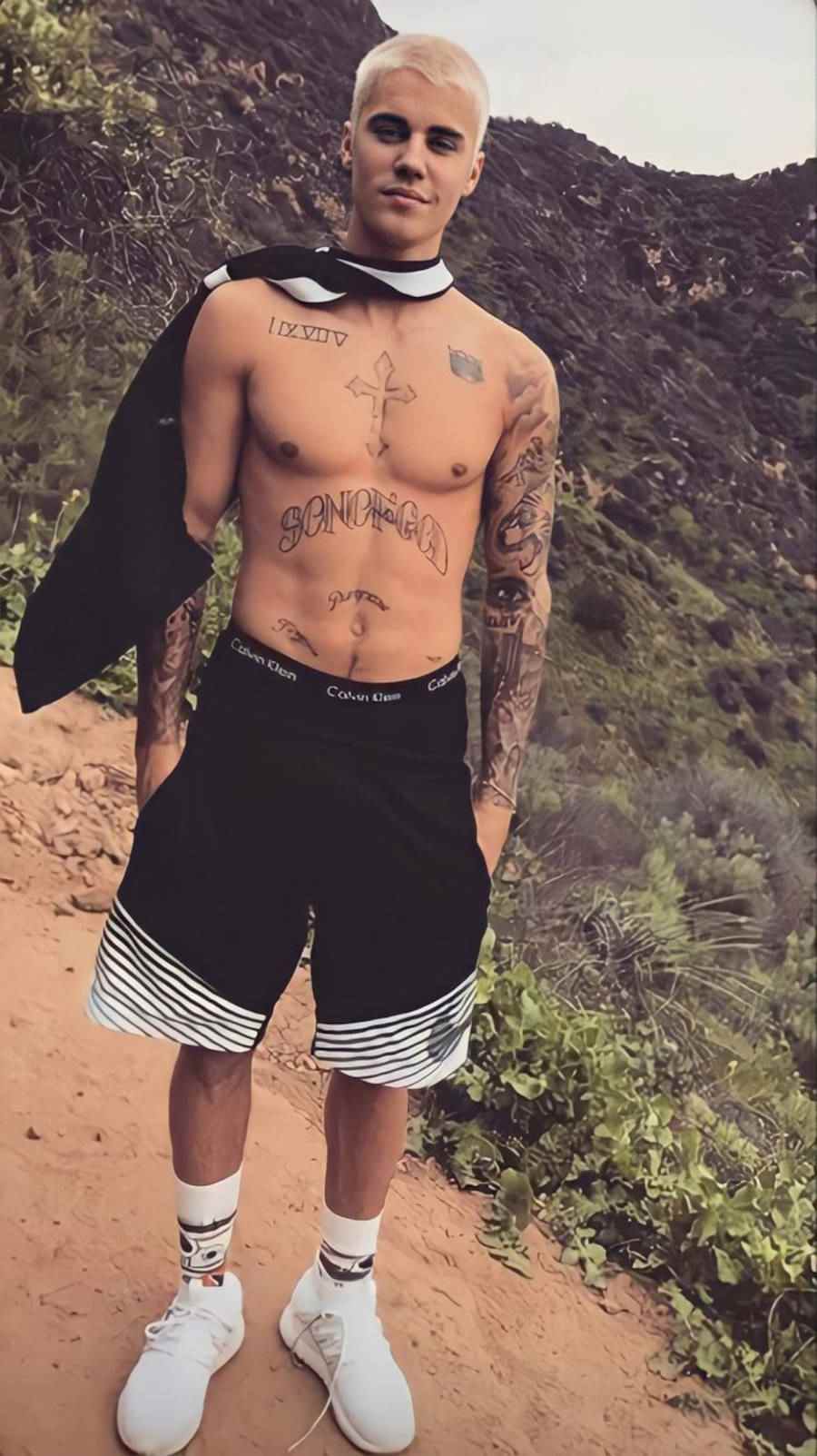 Foto de Justin Bieber no alto de uma colina e o destque é a sua tatuagem "Son of God"
