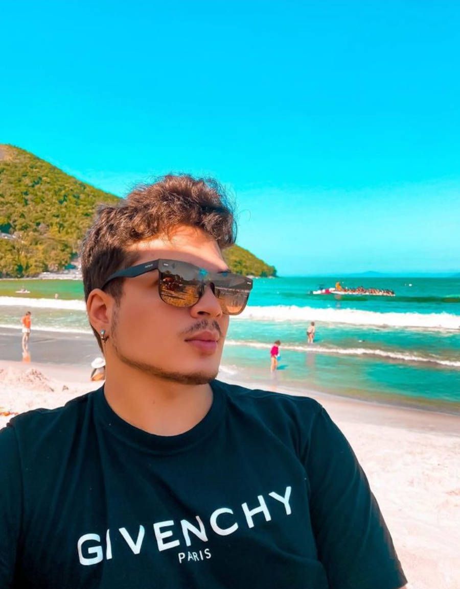 Foto de Lucas Santos na praia com blusa da givenchy e óculos escuro