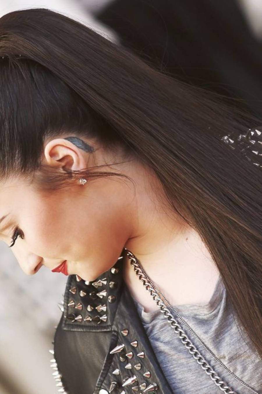 Foto de Demi Lovato de lado com a tatuagem de pena atrás da orelha