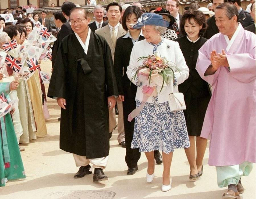rainha em 1999 usando vestido estampado azul com blazer branco e chapéu azul