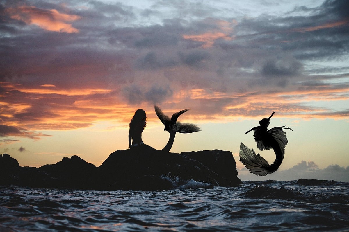 Foto de duas sereias em pedras do mar com céu nublado
