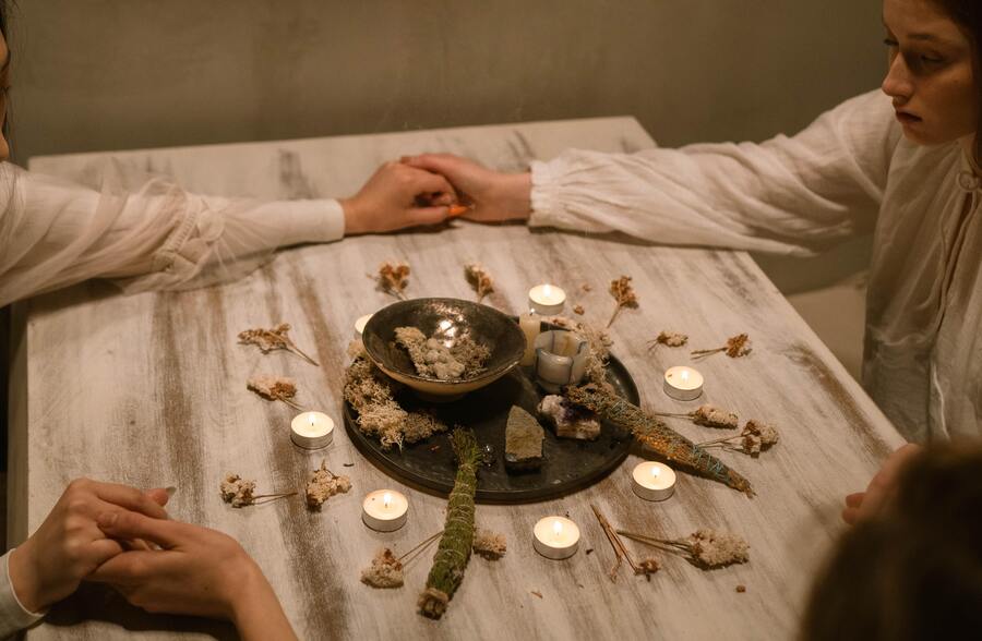 4 mulheres de mãos dadas para realizarem rituais de Ostara com ervas e velas na mesa