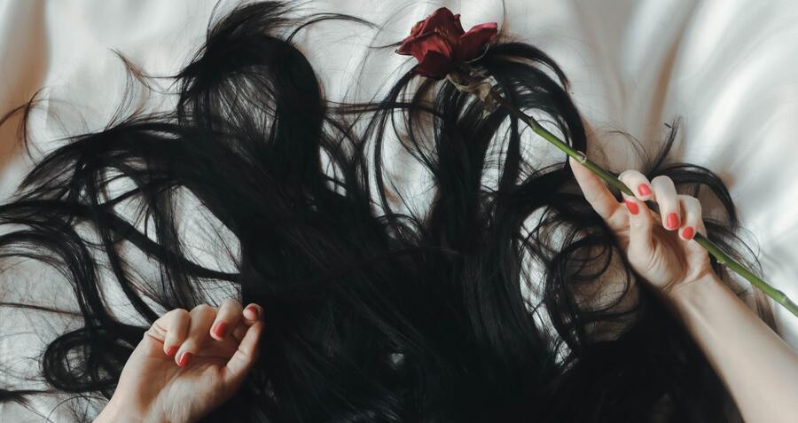 mulher deitada com os cabelos pretos para cima e segurando uma rosa