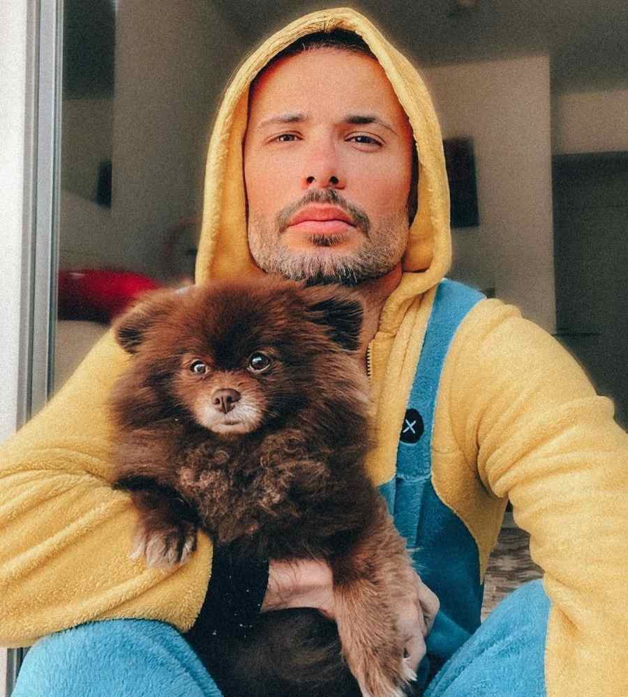 Foto de Alex Gallete com casaco de frio amarelo com touca, segurando cachorrinho Lulu da Pomerânia de cor marrom. 