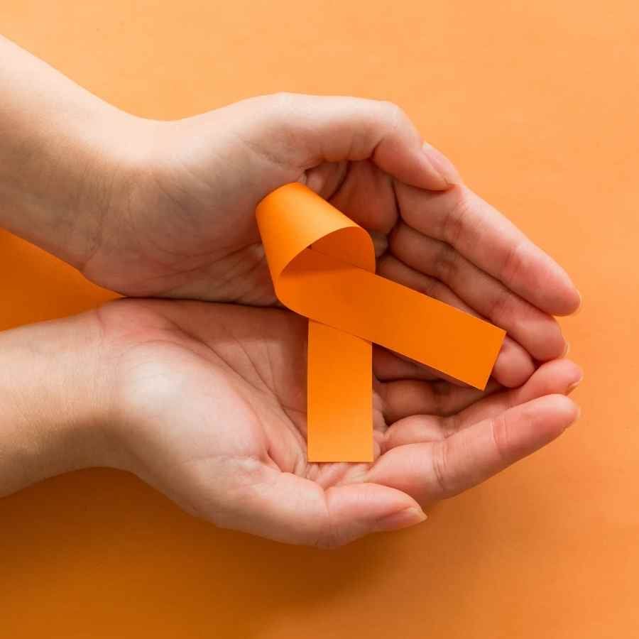 Mãos segurando símbolo laranja da Leucemia Mieloide Crônica.