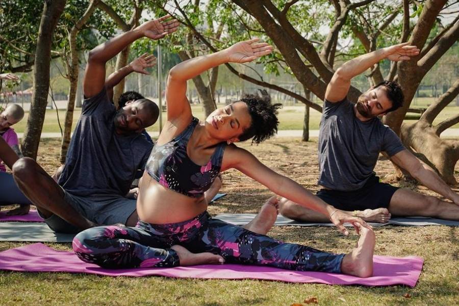 Mulher se alongando em tapete de yoga no parque. Ela usa roupas fitness para grávidas da Oxer