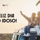 Foto de casal 60+ no pôr do sol em cima de uma van, felizes, com os braços abertos. Ao lado, vemos escrito feliz Dia do Idoso