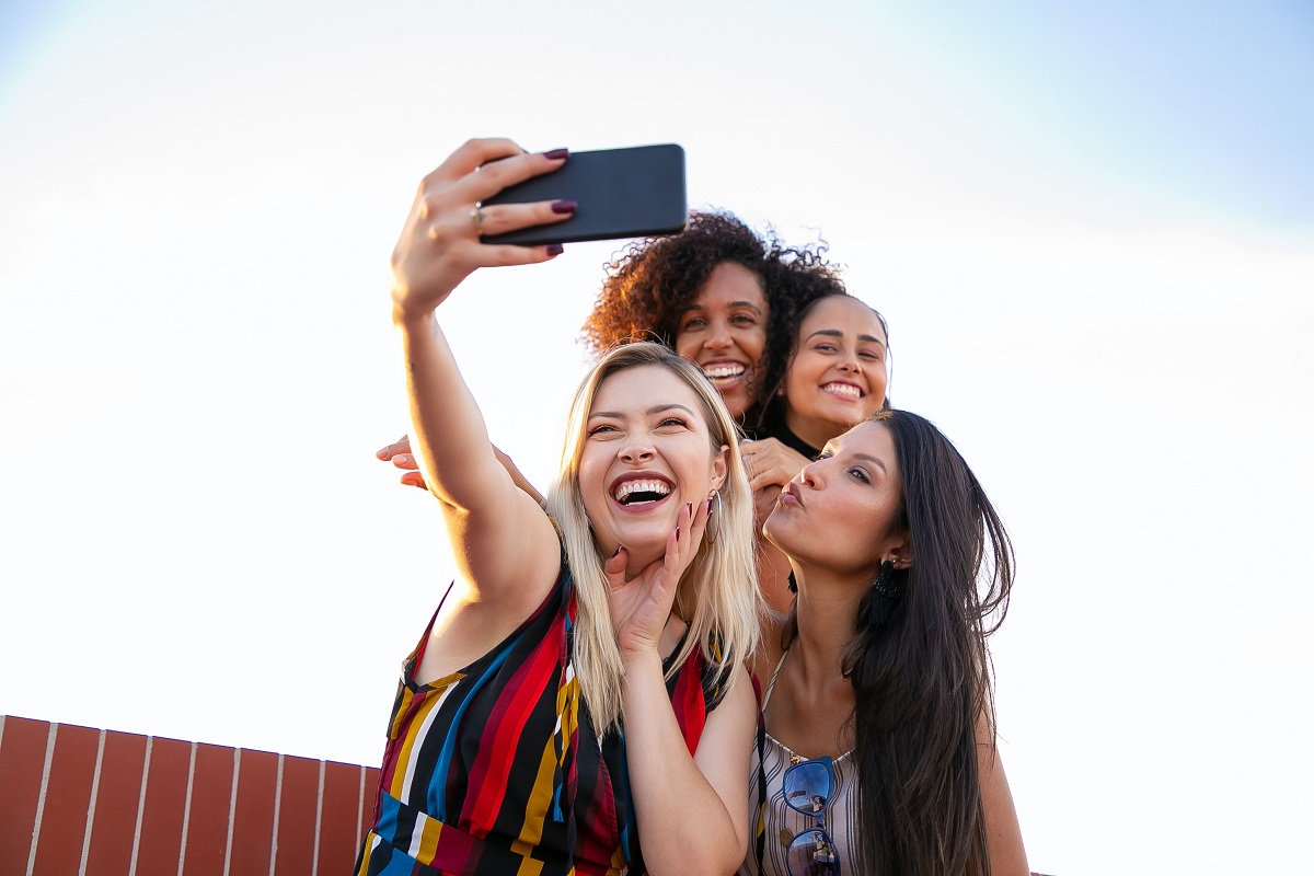 Quatro mulheres tirando uma selfie sorrindo ao ar livre
