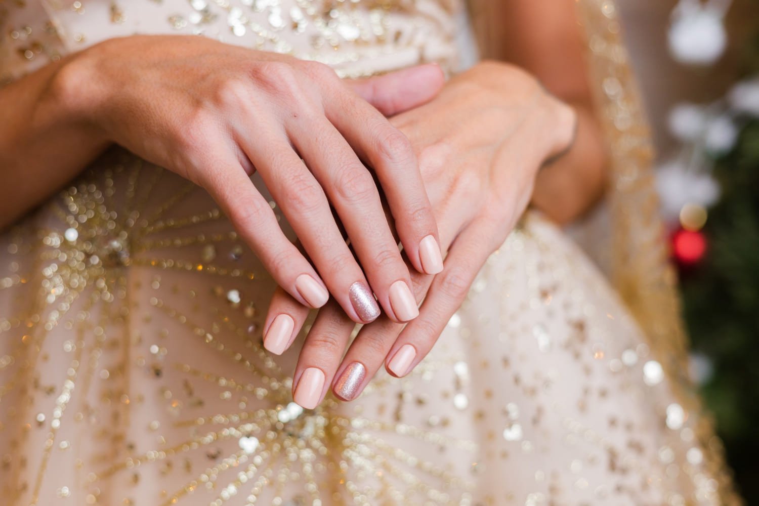 Mulher com as mãos sobrepostas. Suas unhas estão pintadas de uma cor clara enquanto apenas a do dedo anelar segue um tom mais metálico