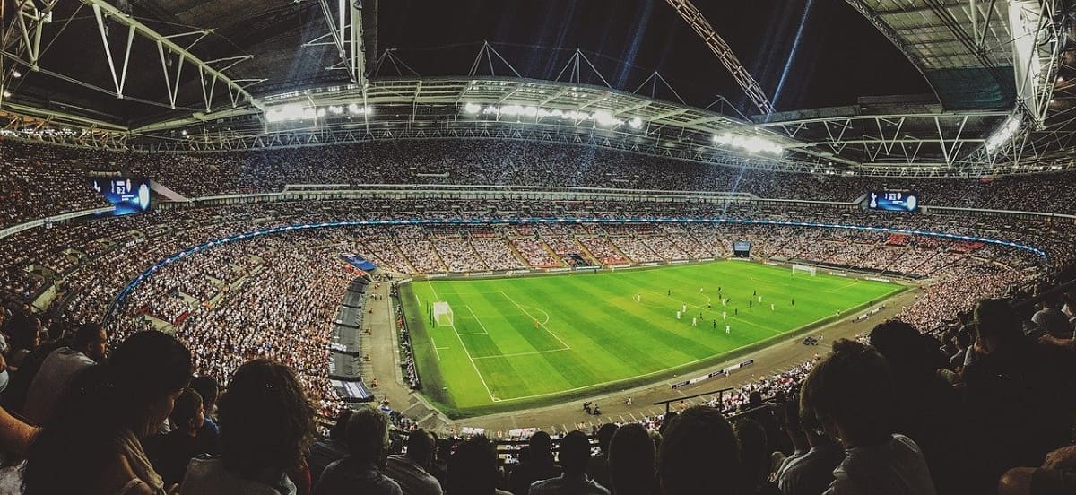 Foto de um estádio iluminado lotado de torcedores que acompanham uma partida de futebol noturna