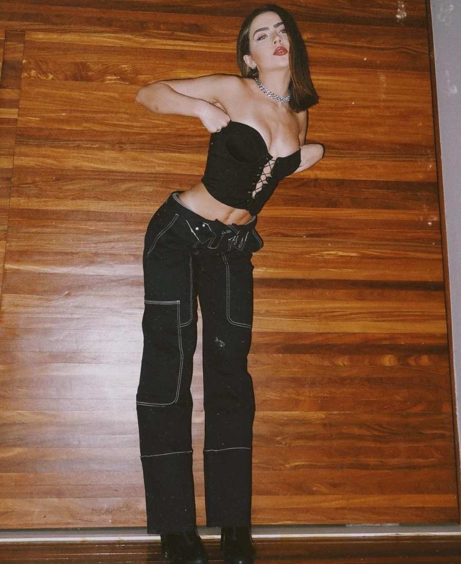 Foto de Jade Picon em pé usando calça cargo e cropped preto com amarrações no decote. 