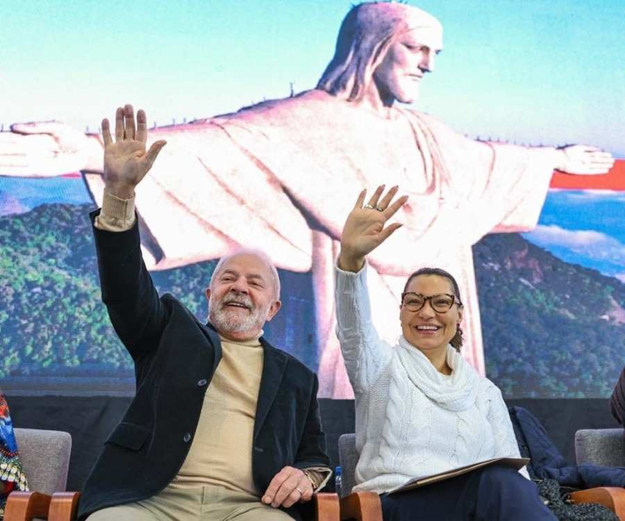 Foto de Lula e Janja sentados em cadeiras com foto do cristo redentor no fundo.