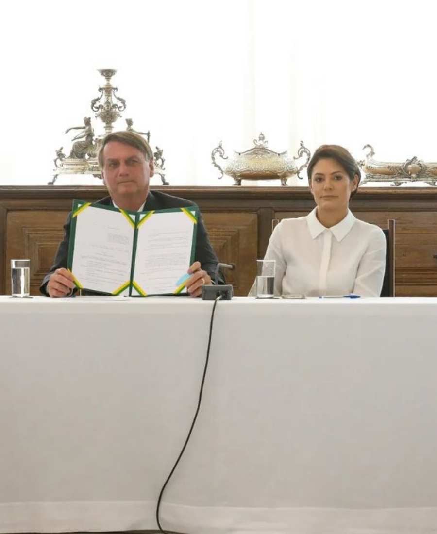 Foto de Bolsonaro e Michelle sentados em bancada. 