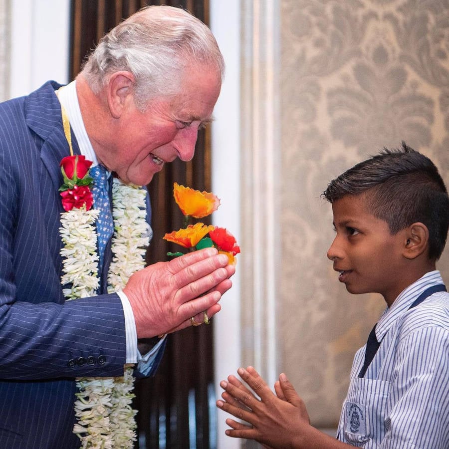 Rei Charles III e menino indiano se cumprimentando.