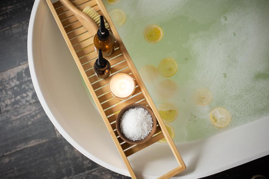 banho para fechar ciclos em uma banheira cheia de água, rodelas de laranja e um apoio de madeira com sabonetes dentro de vidros âmbar e sais de banho
