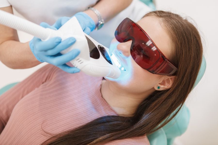dentista aplicando luz especial nos dentes de uma mulher que usa óculos escuros