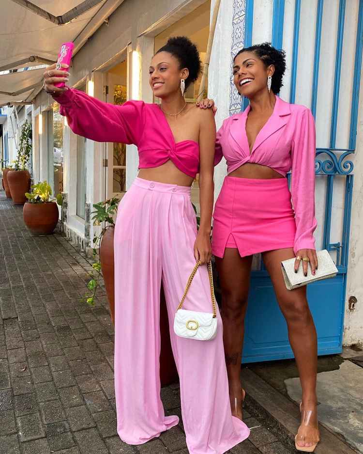 duas mulheres com roupa toda rosa, esquerda calça e top, e da direita saia e top
