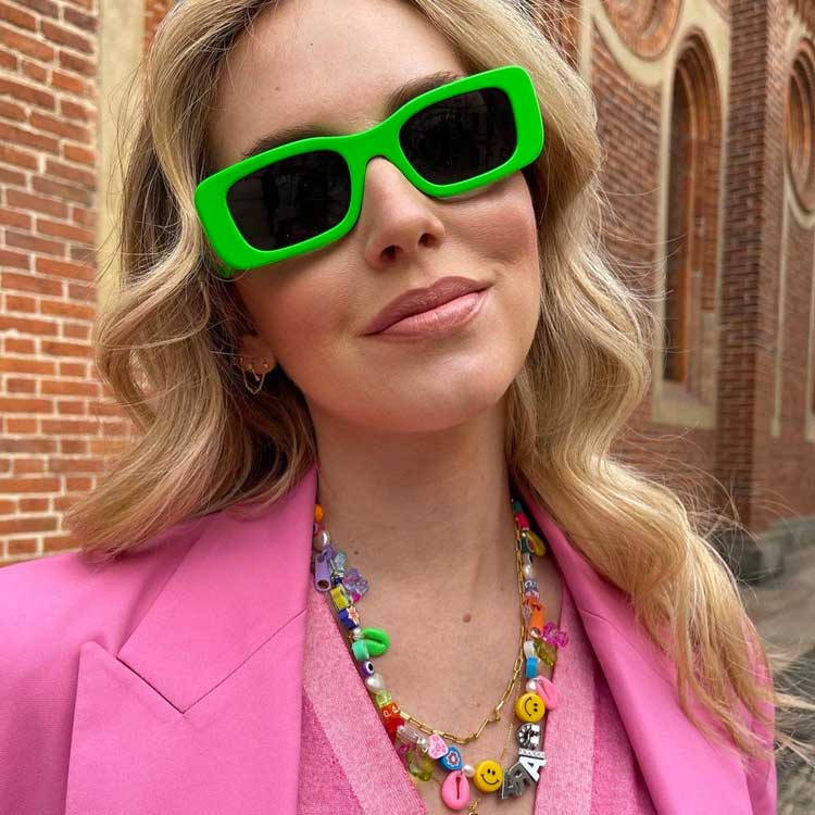 mulher loira de óculos de sol verde, colar de miçangas anos 2000 e look rosa