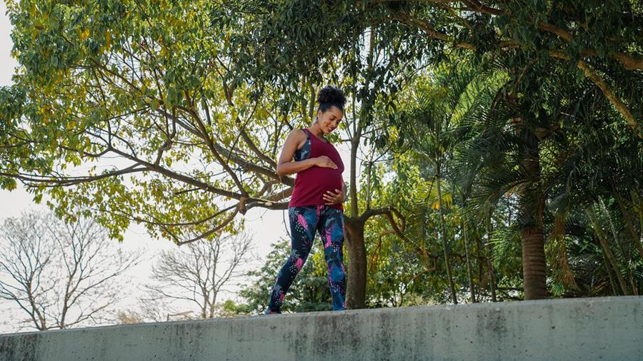 Mulher grávida fazendo caminhada em parque usando top, legging e camiseta regata Oxer
