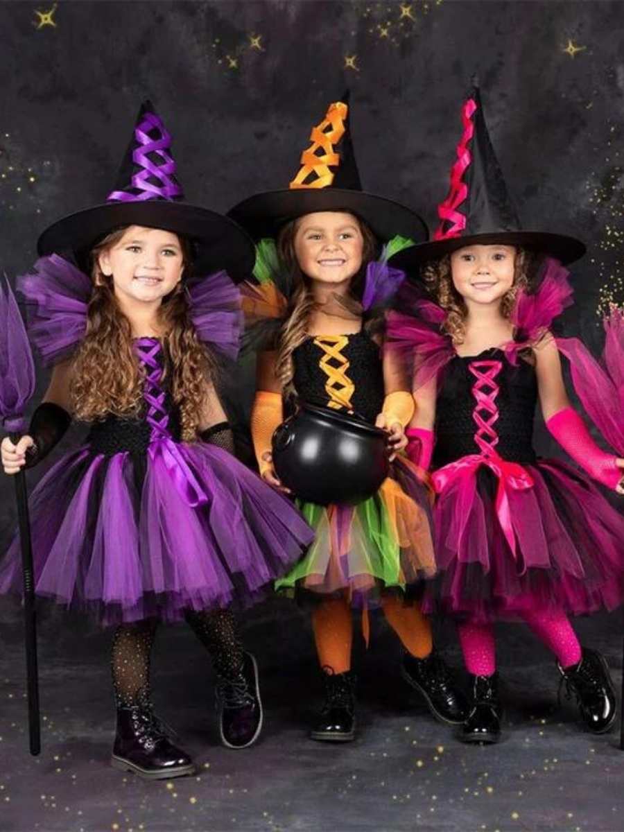 Foto de 3 meninas crianças vestidas com fantasia de bruxa. Cada vestido possui uma coloração diferente: preto e roxo, preto e rosa e preto e abóbora com verde.