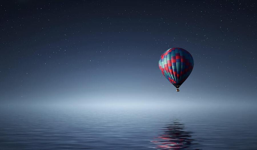 um balão sobrevoando o mar em uma noite de lua nova com céu estrelado
