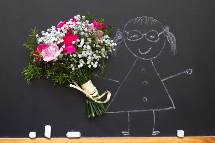 Foto de desenho de menina em quadro de giz, com buquê de flores colado na mão da boneca.