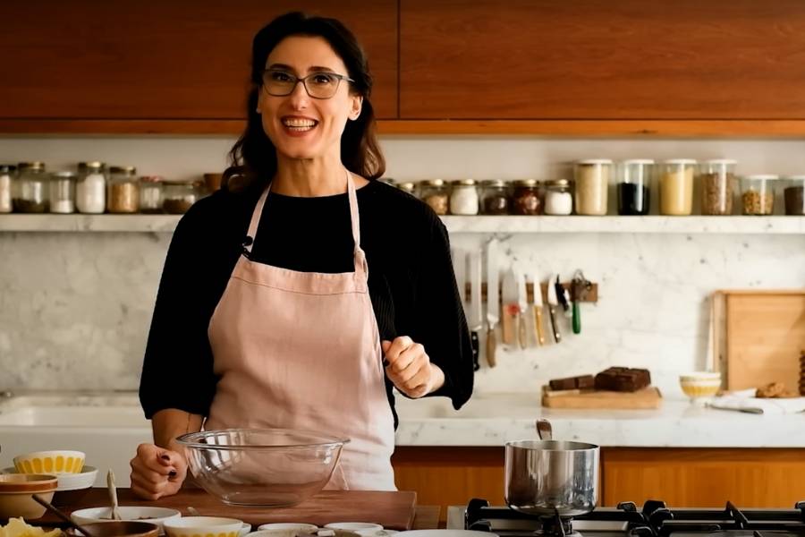 Print de vídeo com Paola Carossela, chef de cozinha, na cozinha de sua casa preparando algum prato. 
