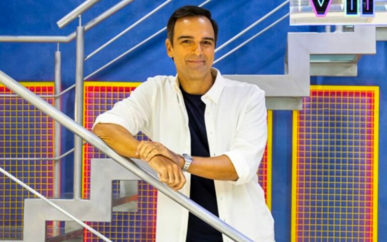 Foto de Tadeu Schmidt sorrindo na escada do BBB para ilustrar a matéria de quanto os participantes do BBB ganham por semana