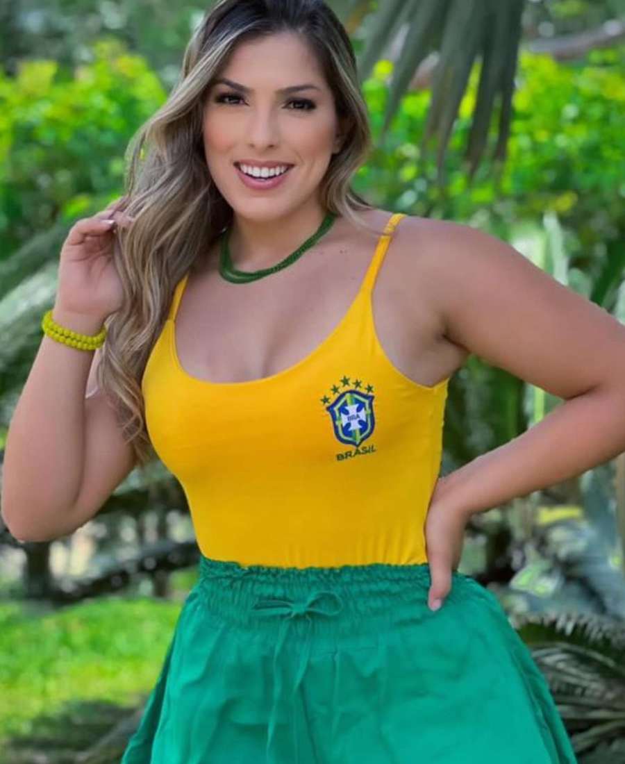 Imagem com fundo de plantas. No centro, mulher usando roupa copa do mundo: body amarelo do Brasil + short verde.