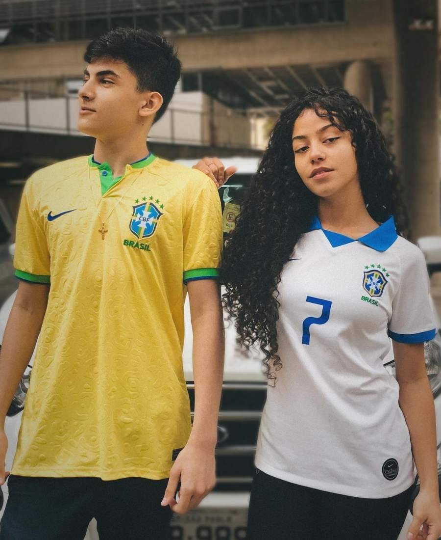 Imagem com fundo de carro. No centro, casal usando roupa copa do mundo: camiseta amarela e branca do Brasil.