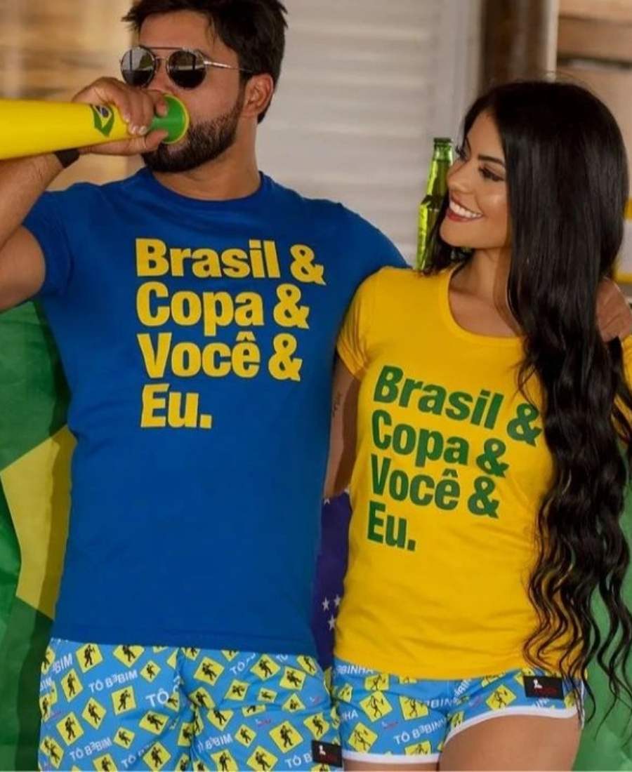 Imagem com fundo de bar. No centro, casal usando roupa copa do mundo: camiseta azul e amarela, ambas escrito "Brasil & Copa & Você & Eu".