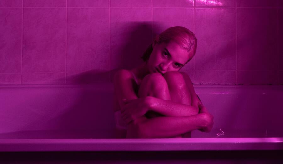 mulher loira de cabelo curto em uma banheira com luz rosa