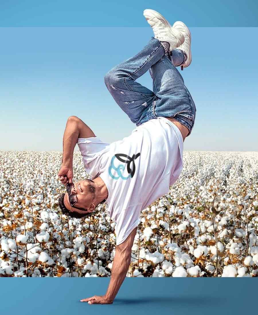 Imagem com fundo de campo de algodão. No centro, homem fazendo manobra com uma mão só no chão, usando roupas feitas de algodão sustentável.