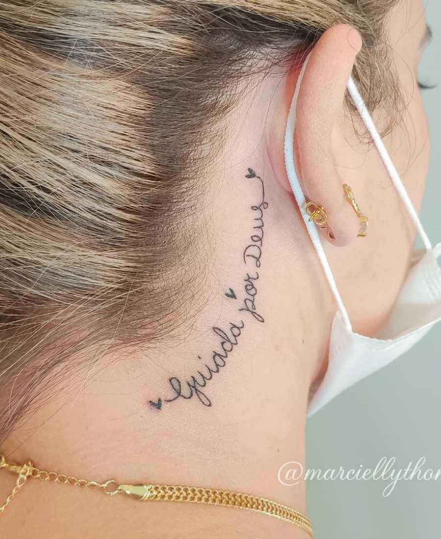 Foto de tatuagem de frase religiosa atrás da orelha de uma pessoa.