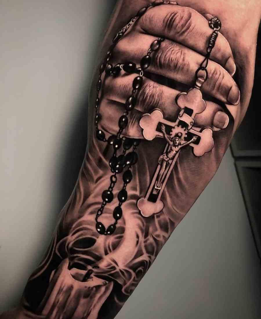 Foto de tatuagem religiosa realista com mão segurando terço.