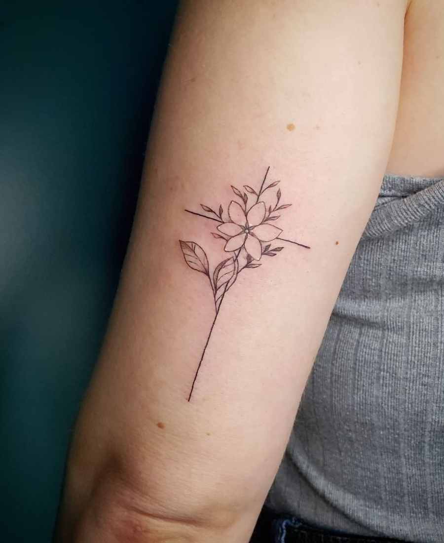 Tatuagem de uma cruz com flores no braço de uma pessoa.