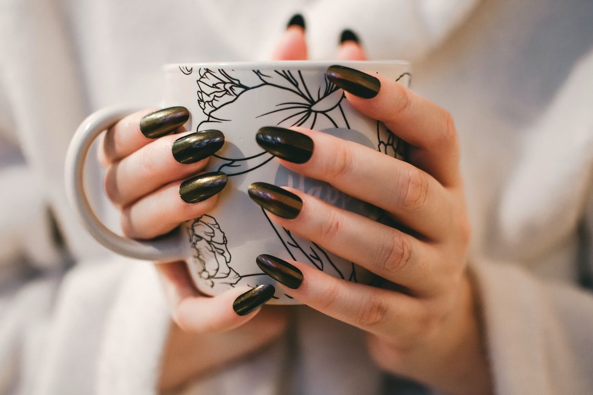 mulher com unhas pretas segurando uma xícara de café com as duas mãos