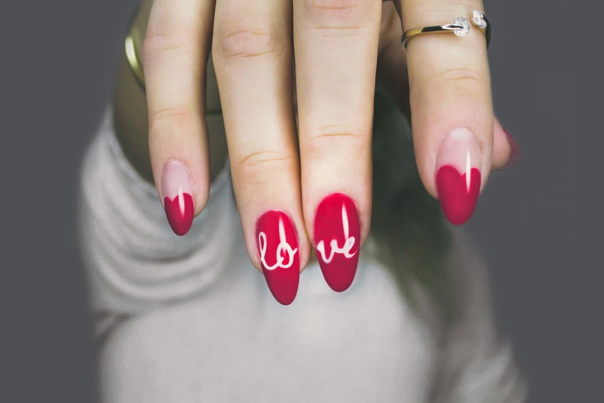 mulher mostrando uma das mãos onde suas unhas estão pintadas de vermelho e escrito love em dois dedos