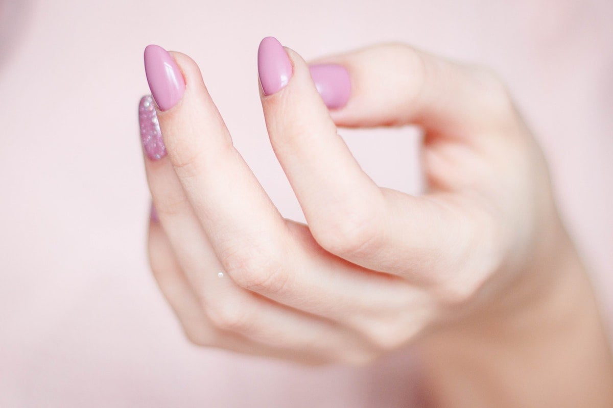 mão feminina destacando as unhas feitas e pintadas de lilás