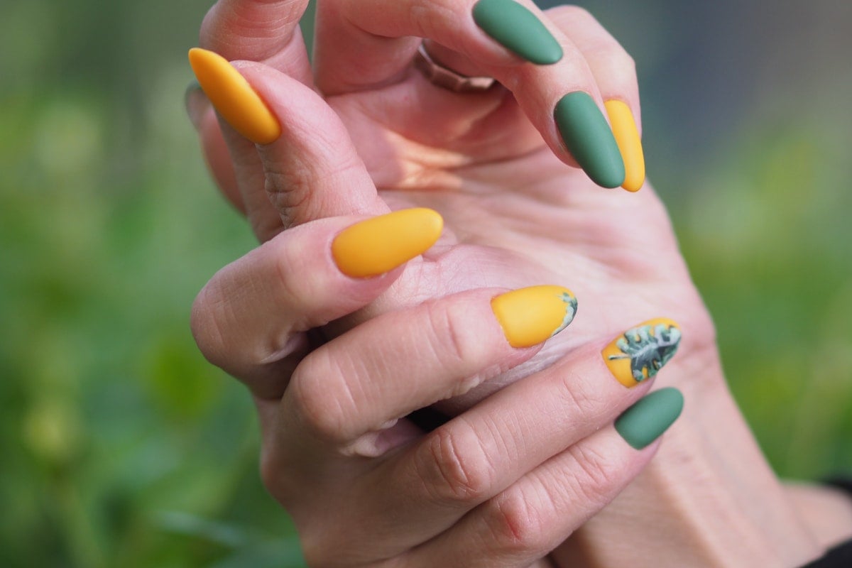 mãos femininas em destaque com as unhas pintadas em verde e amarelo de forma alternada