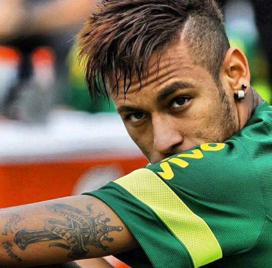 Foto de Neymar olhando de lado parra câmera com foco em sua tatuagem de cruz com coroa
