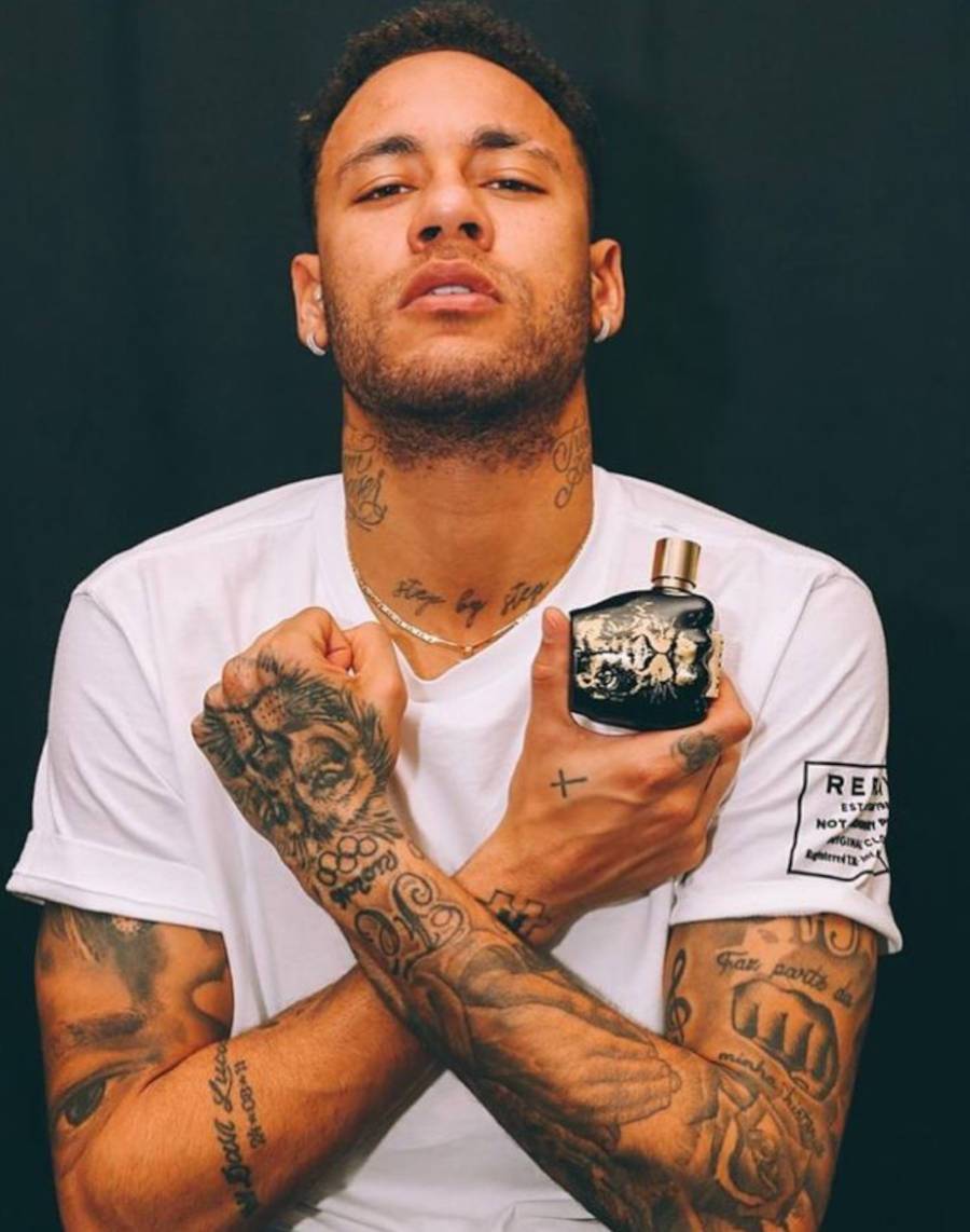 Foto de Neymar segurando um frasco de perfume com os braços tatuados