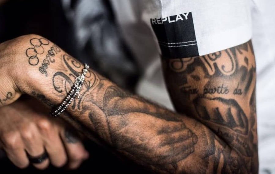 Foto do braço do jogador da seleção brasileira com a tatuagem de mão e oração e palavra fé