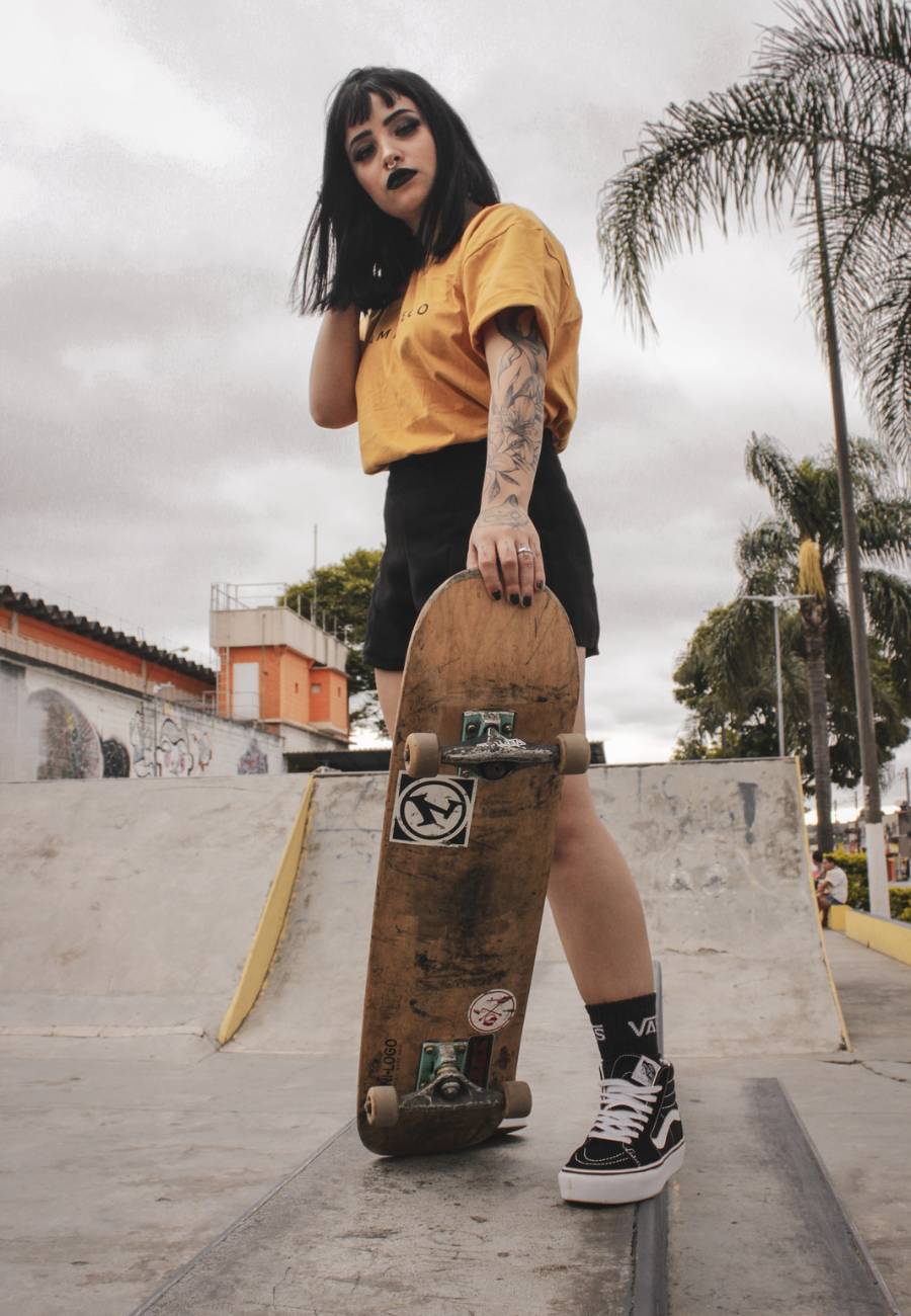 mulher usando camiseta amarela, shorts preto e tênis para skate da Vans de cano alto