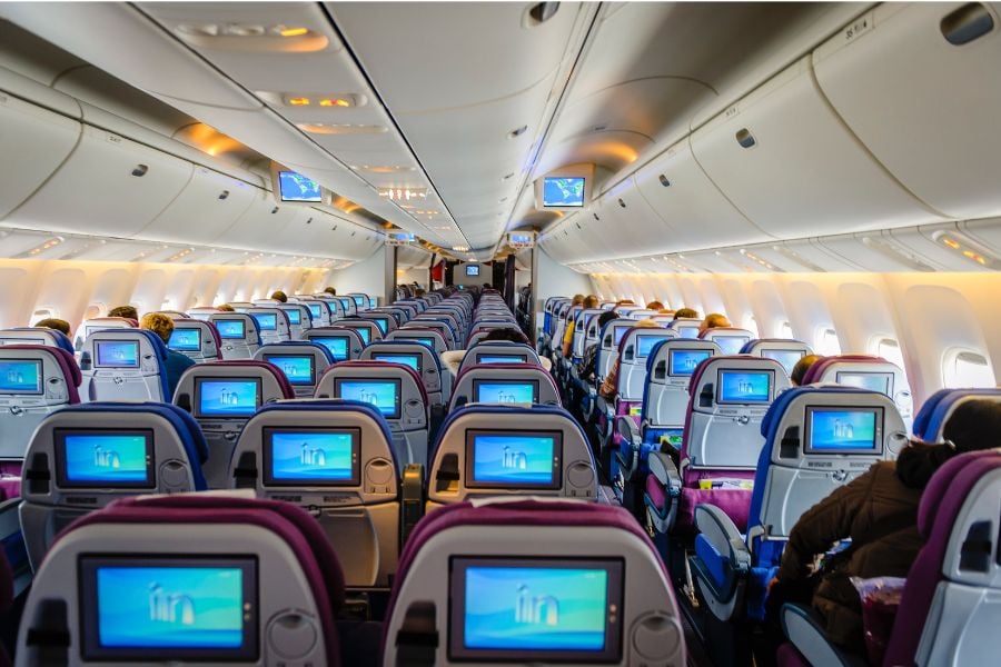 foto de interior de avião com poltronas e TVs na parte de trás dos assentos