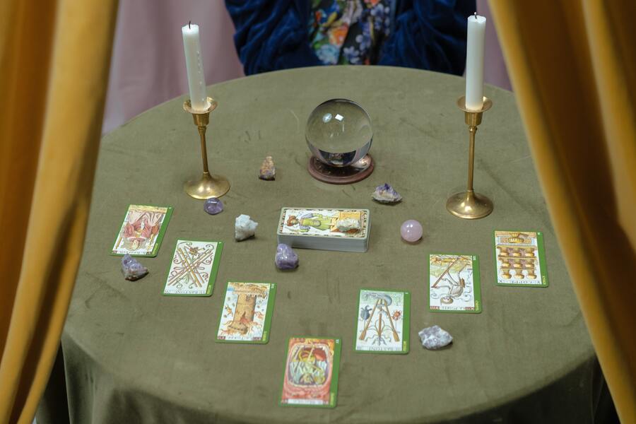 mesa com toalha, bola de cristal, cristais, duas velas em castiçais e cartas de tarot espalhadas