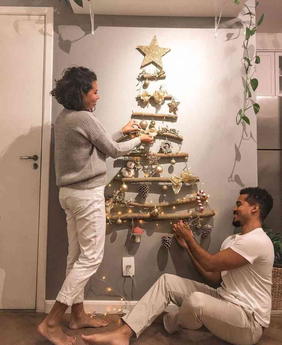 Foto de casal decorando árvore de natal de galhos na parede.