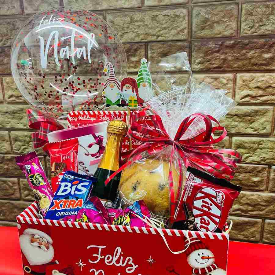 Foto de caixa vermelha com biscoitos, panetone, chocolates e bebida.