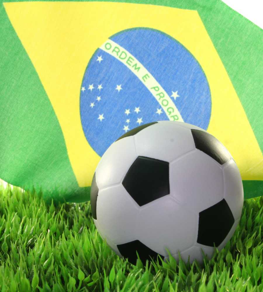 Imagem de bolsa de futebol em gramado com bandeira do Brasil no fundo - jogos do Brasil na Copa 2022.
