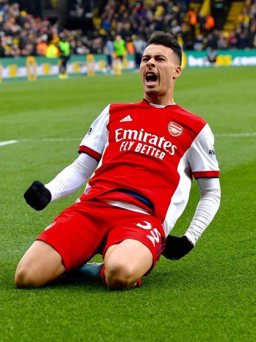 Imagem de Gabriel Martinelli agachado em estádio comemorando gol de seu time Arsenal. 